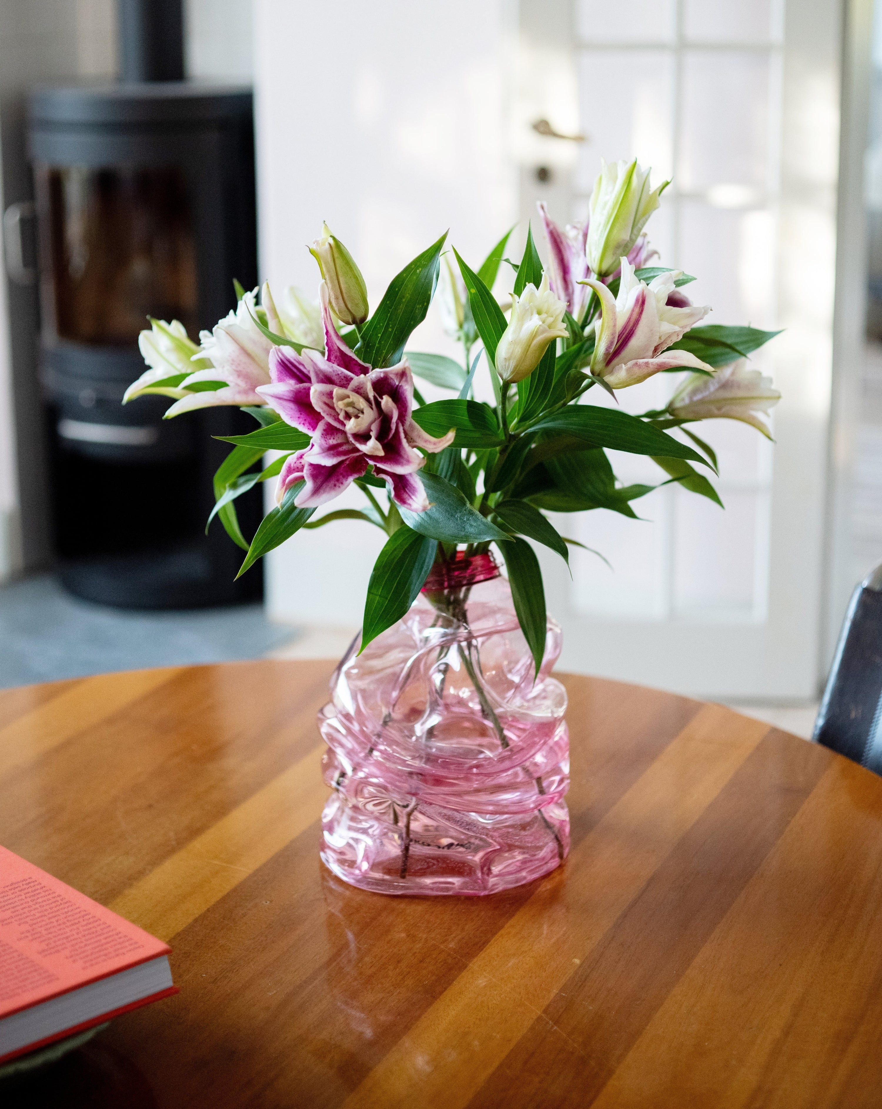 Medium pink handmade recycled plastic vase with pink lillies on the table background