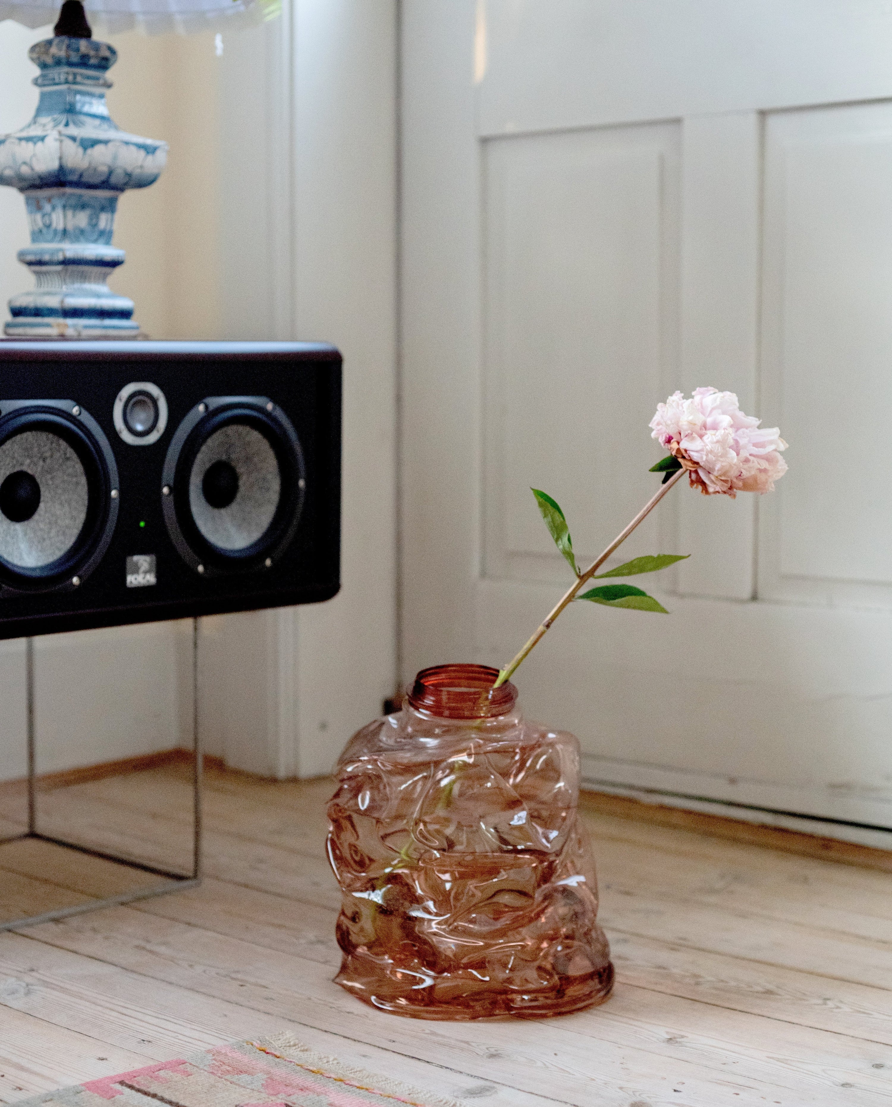 Medium brown handmade recycled plastic vase with pioneer flower on the floor with radio in the corner 