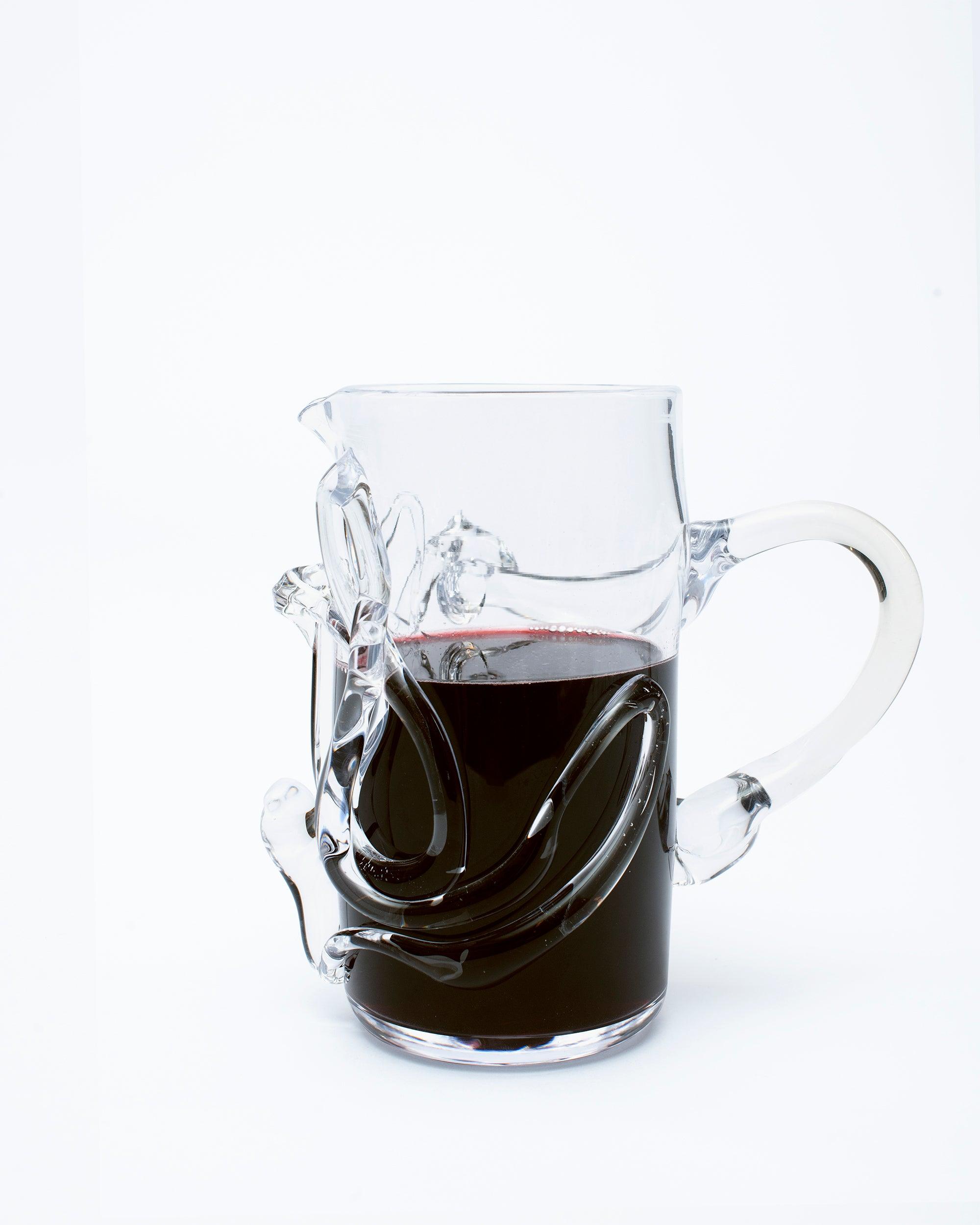 Glass pitcher with melted glass details with handle on the right side with wine on white background