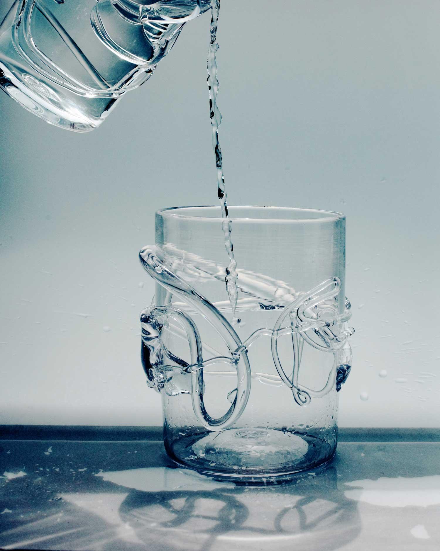 Pouring water into a glass vase with melted glass design on a white and gray shadow background