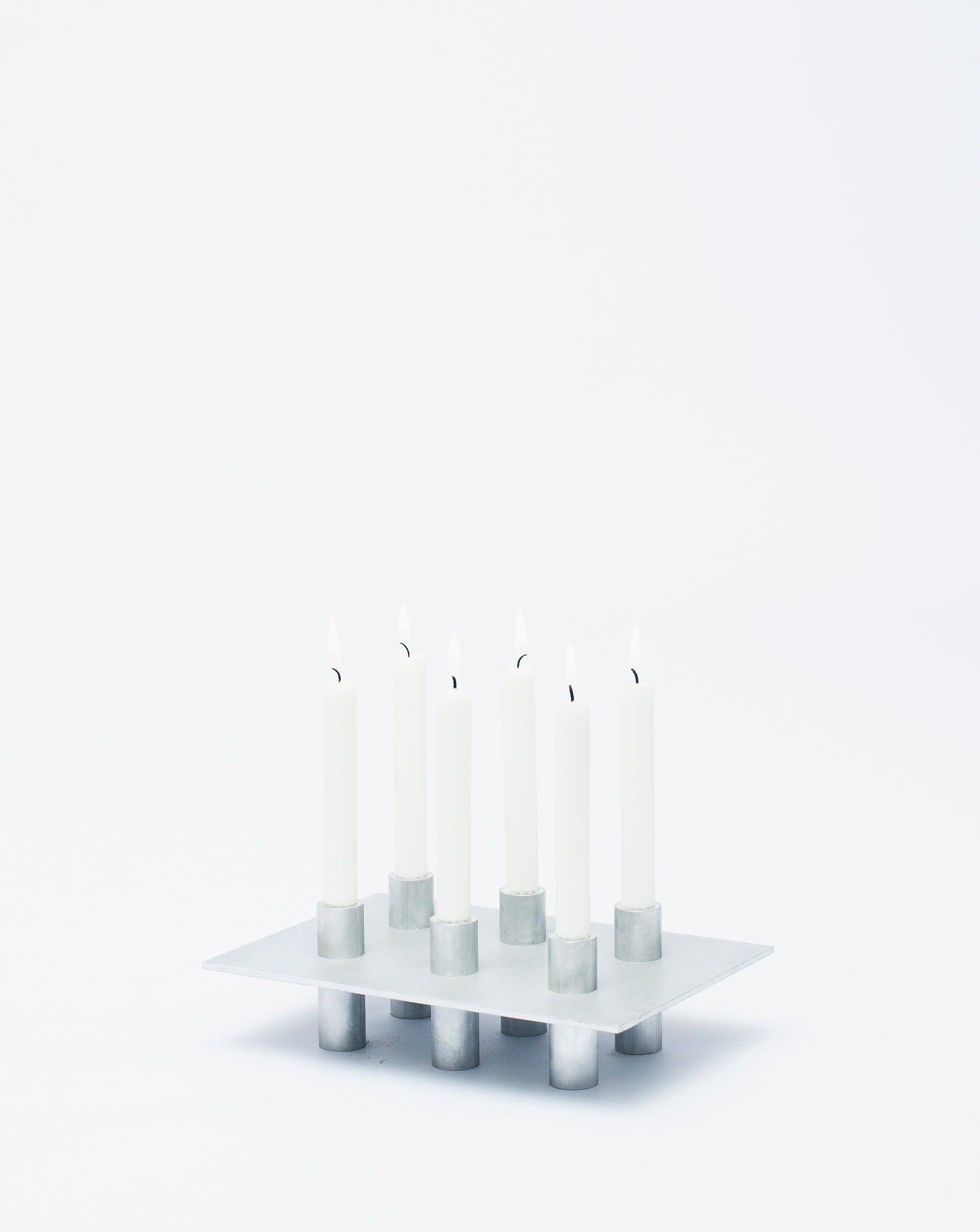 Six lighted candles on an aluminum candlestick P-L series with white background