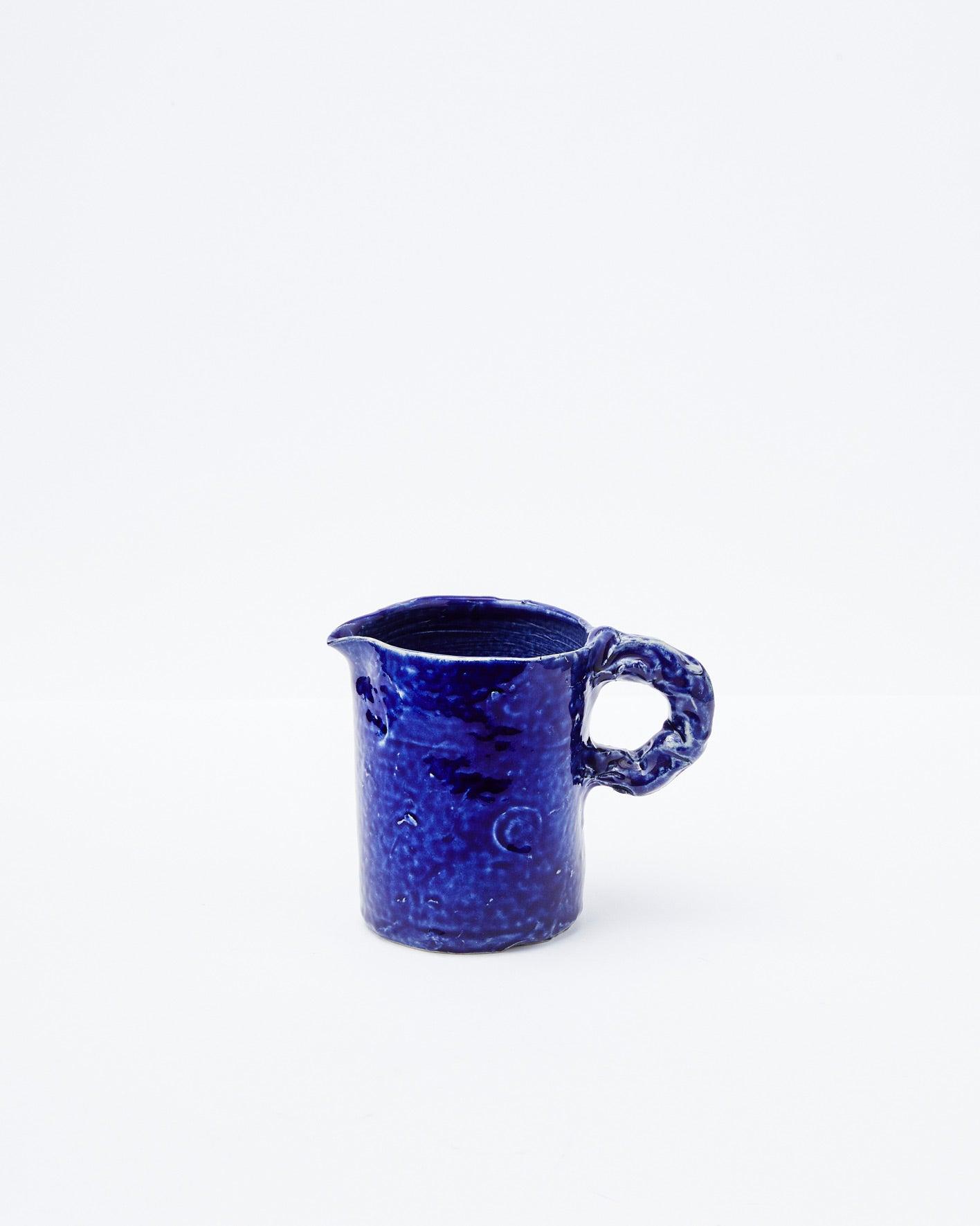 Dark blue modern ceramic pitcher with left-handed handle on a white background