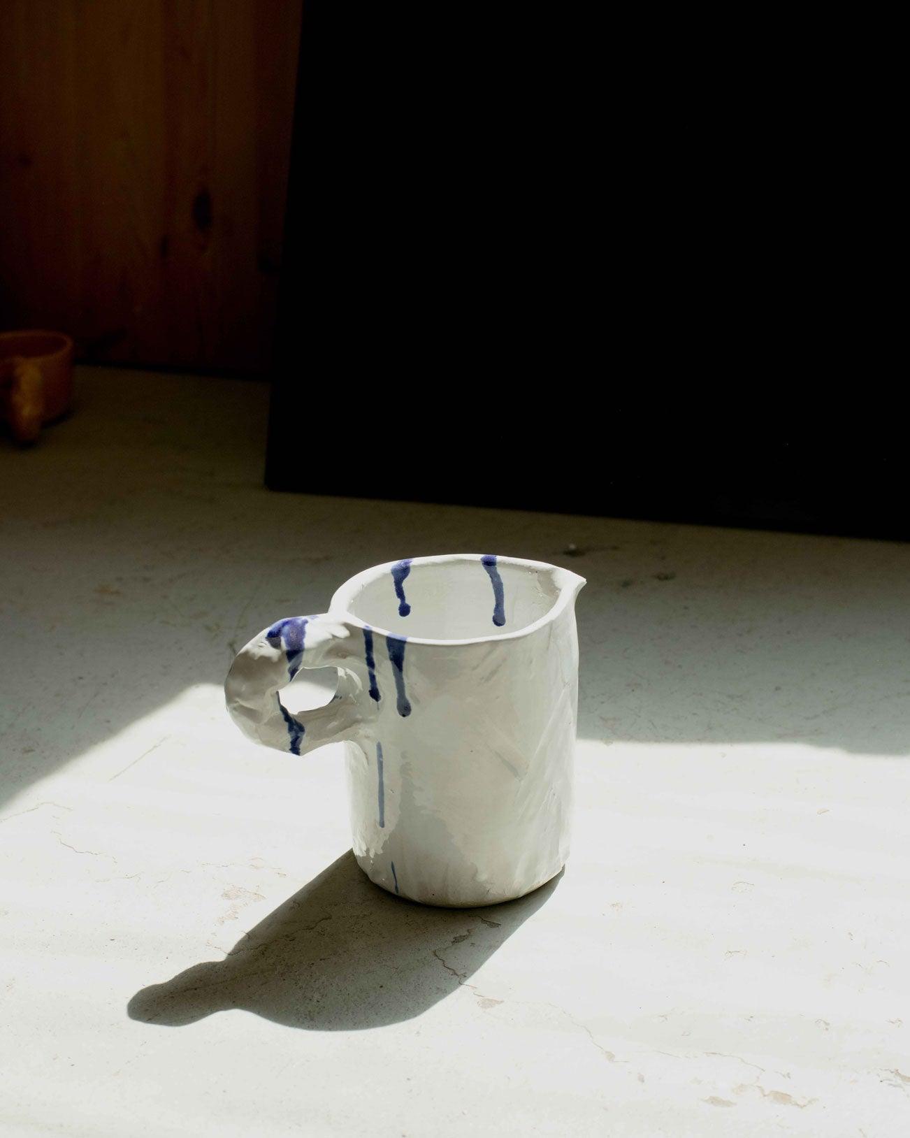 White modern ceramic pitcher with diagonal handle on a light reflexion background