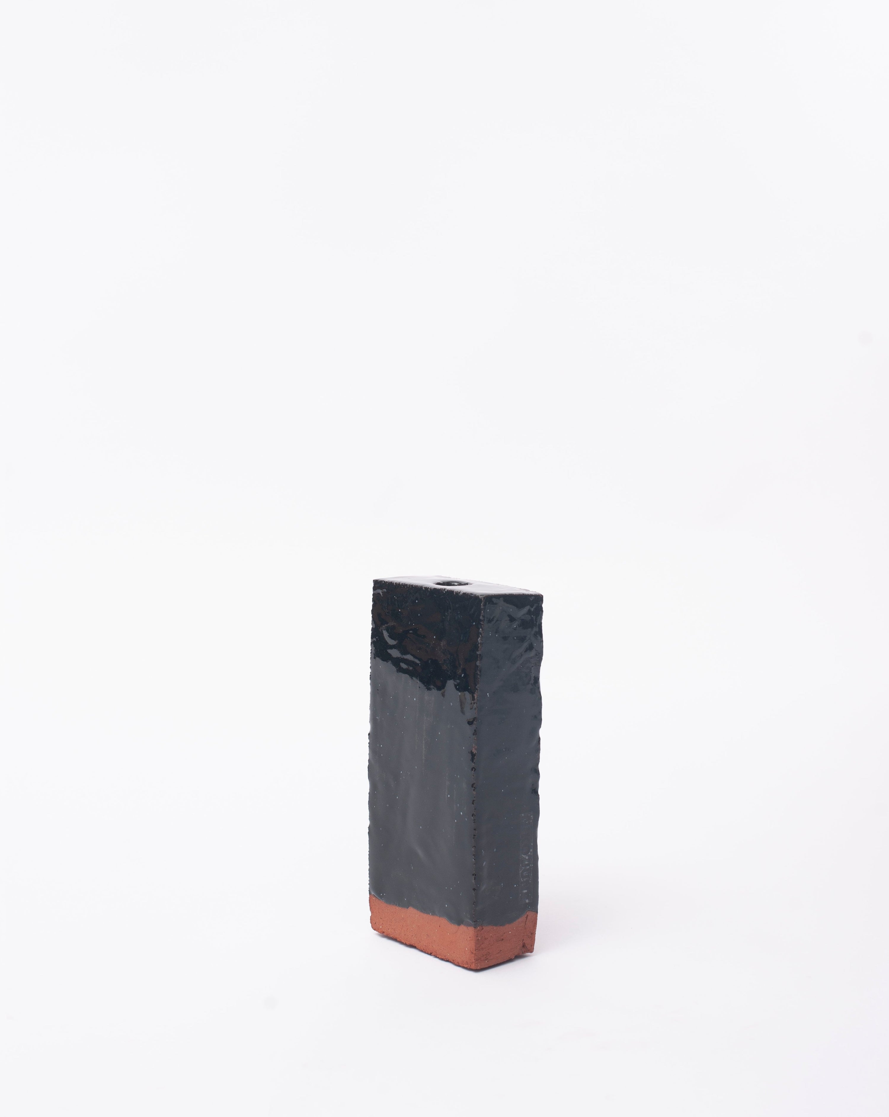 Handmade black brick ceramic candle holder in white glaze in background with right side view
