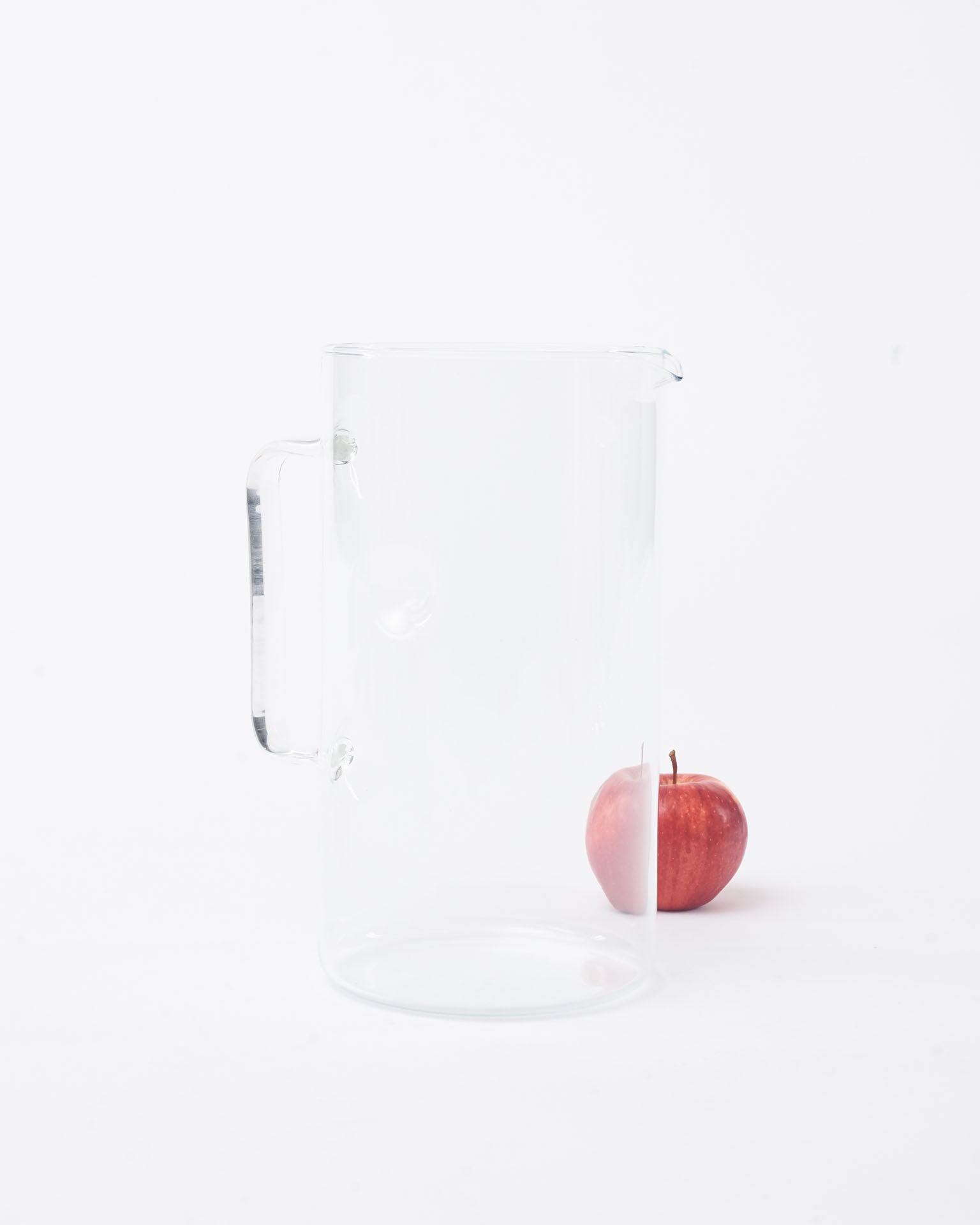 Glass pitcher basic with an apple in back in white background