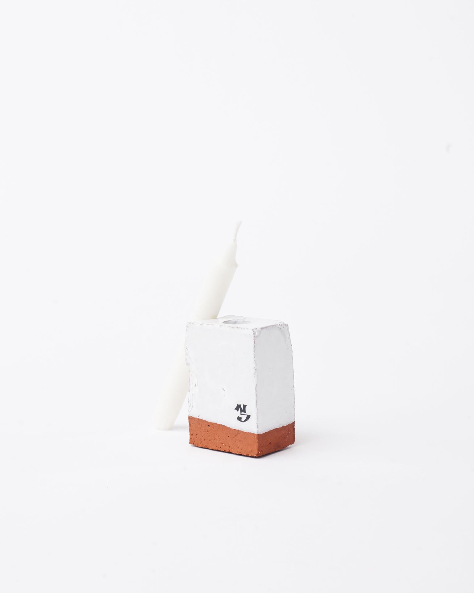 Handmade white brick ceramic candle holder small with candle next to it in white background 