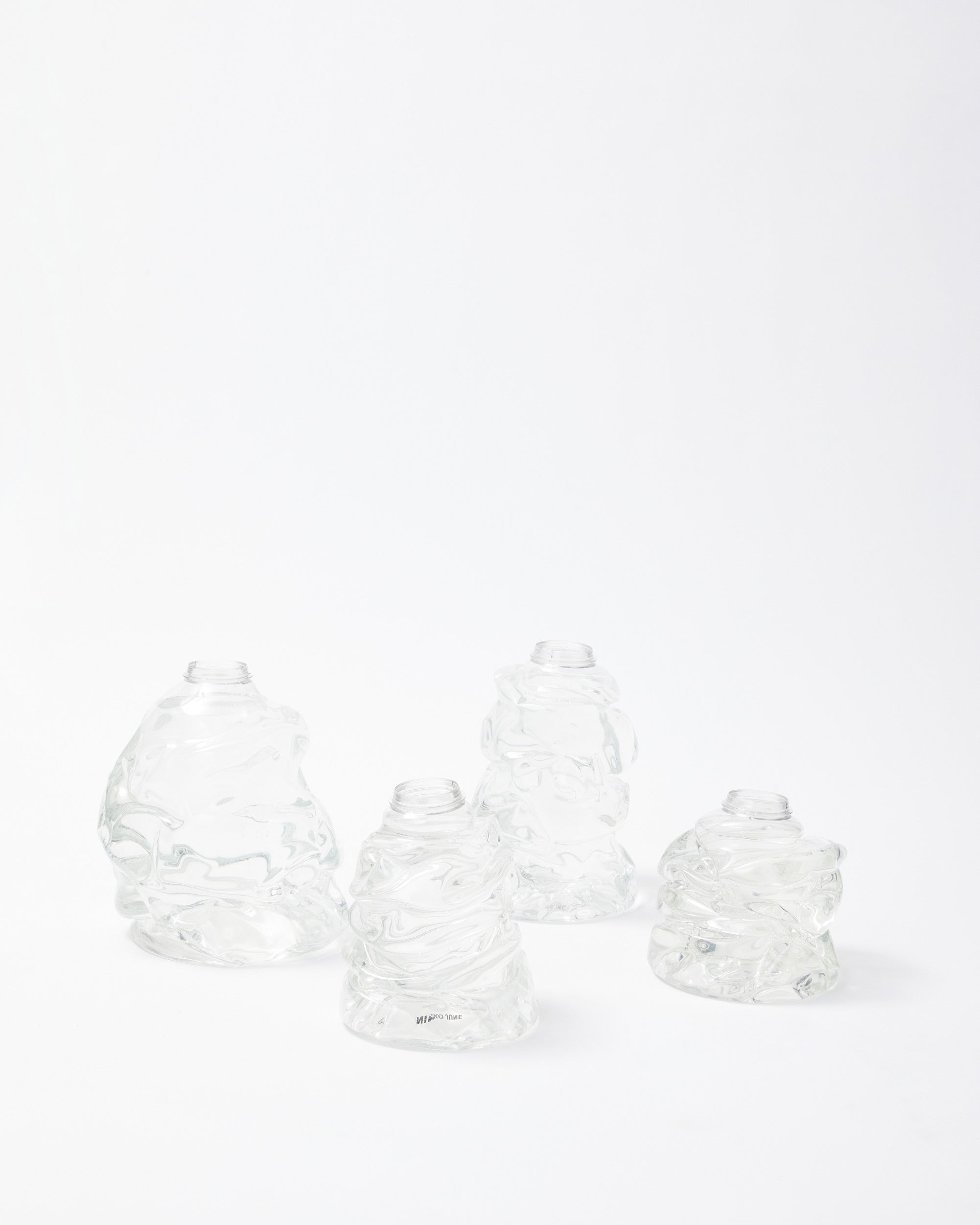 White background, transparent handmade recycled plastic vases of different sizes side by side.
