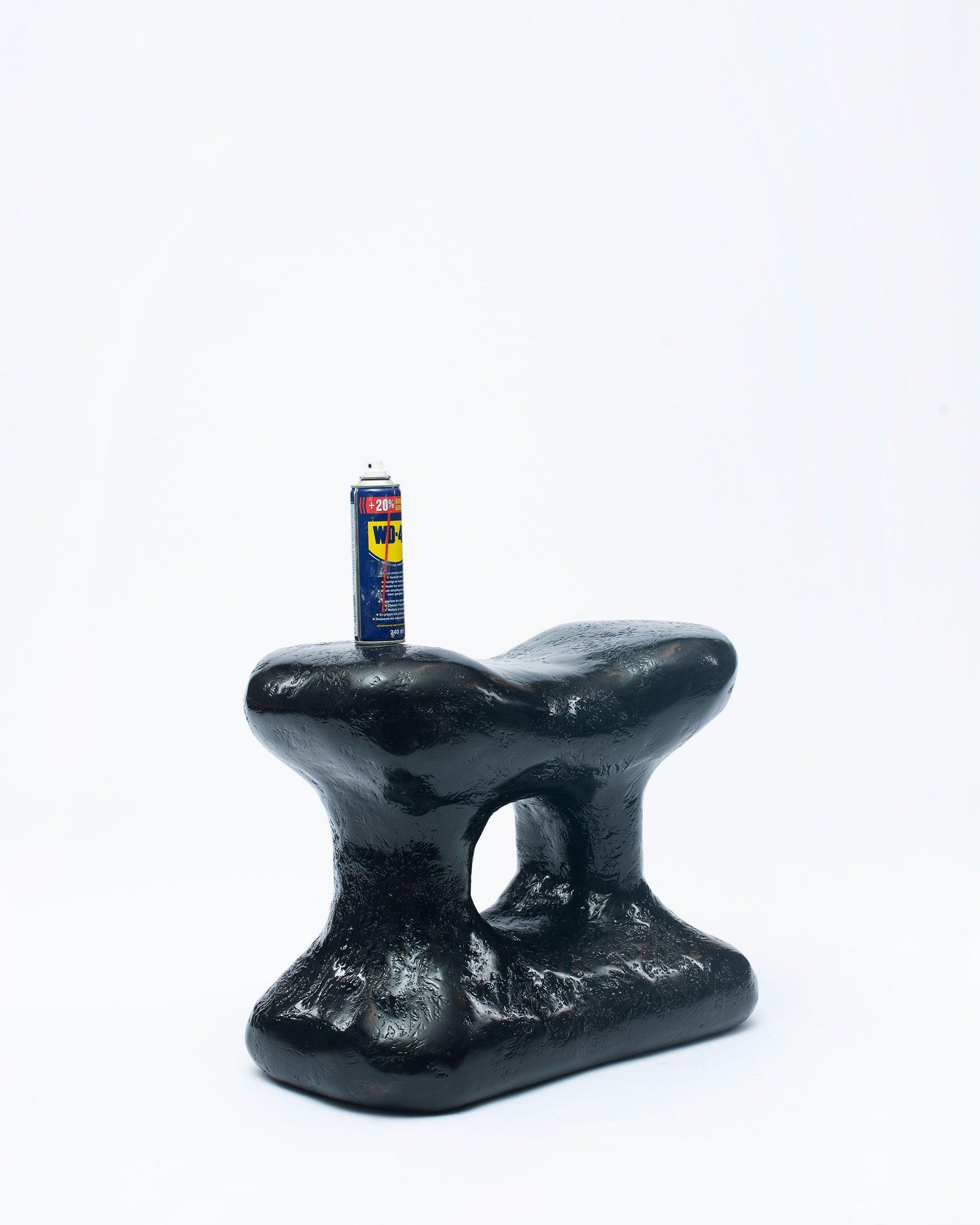 Hand-carved collectible black stool by NIKO JUNE left leaning with sprayed in a corner in white background