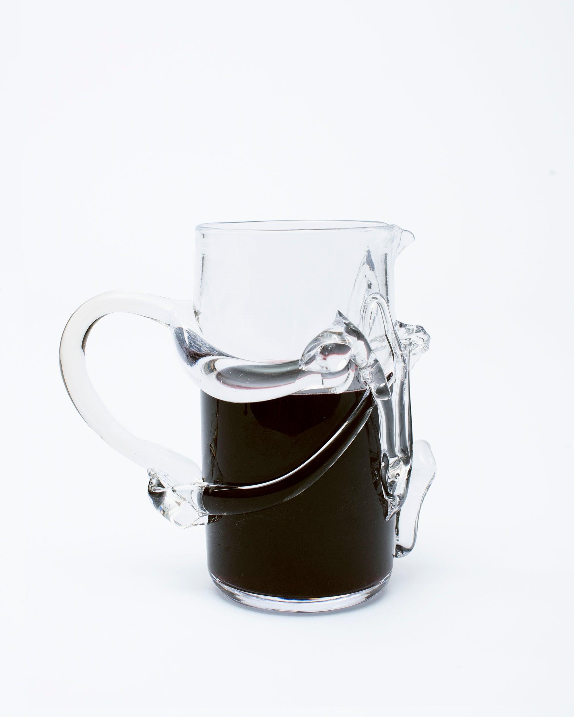 Glass pitcher with melted glass details with handle on the left side with red wine on white background