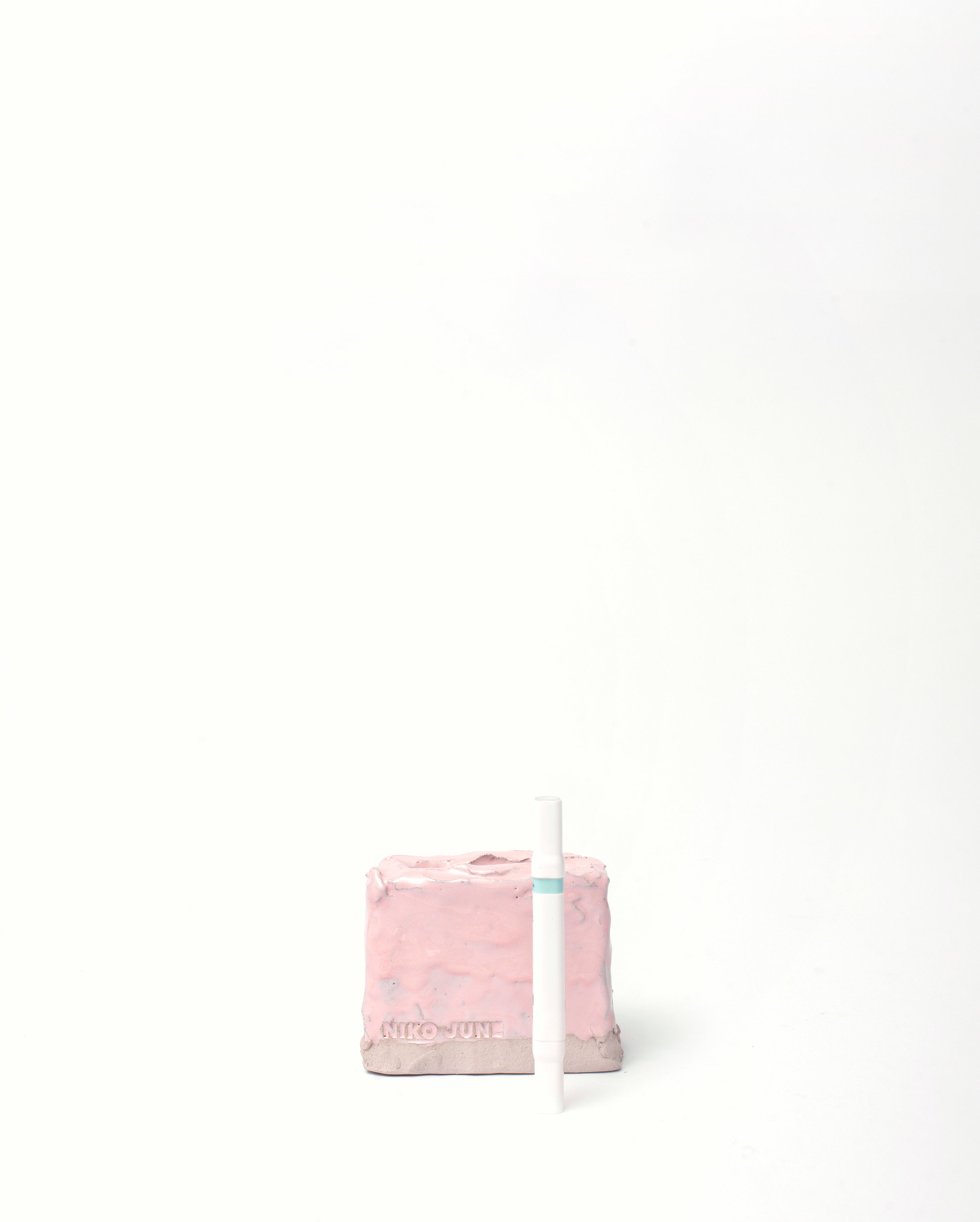 Handmade ceramic organizer object in pink glaze with a white pen facing front in white background