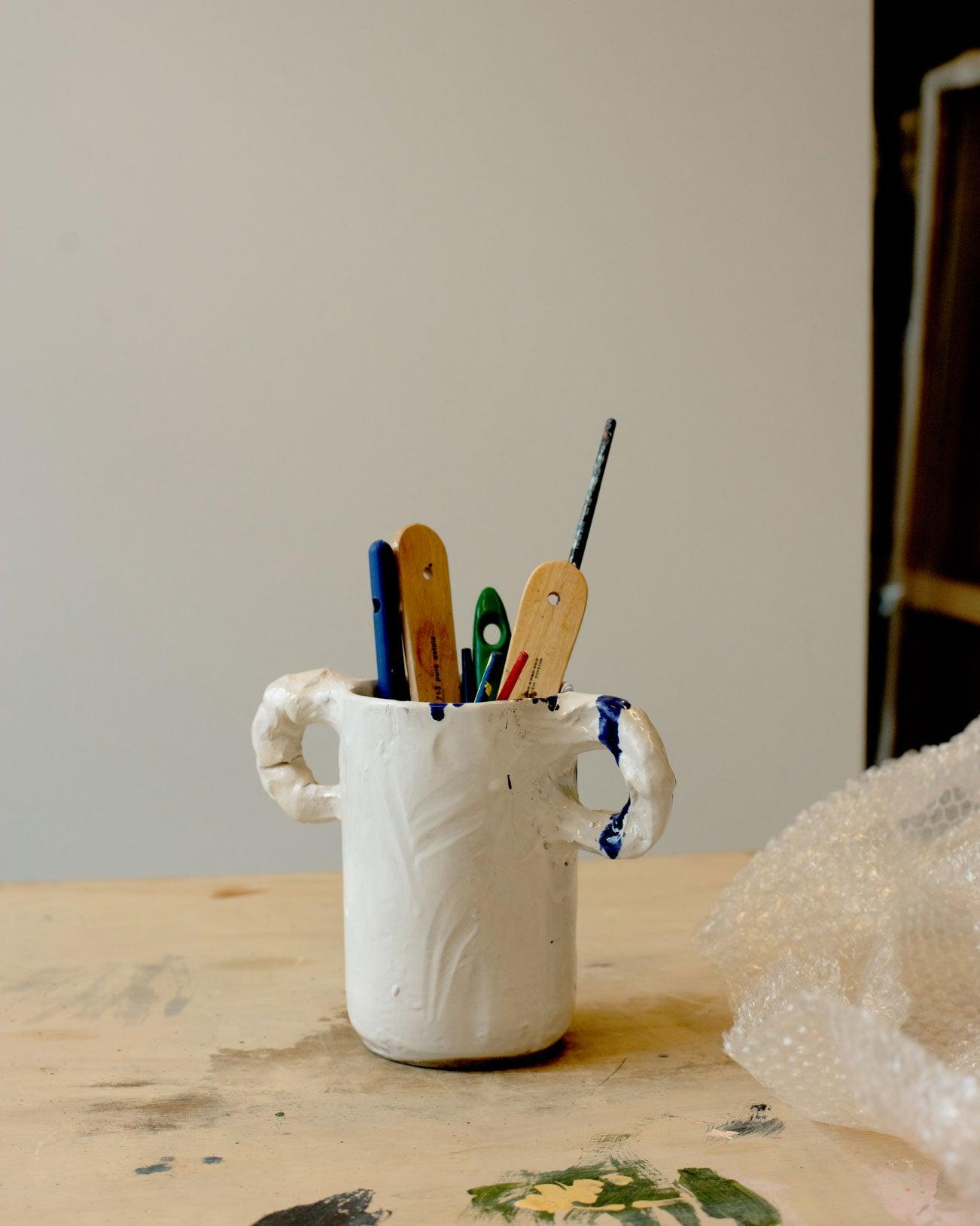 White modern ceramic vase with two handles diagonally positioned and covered with pencils on a white background