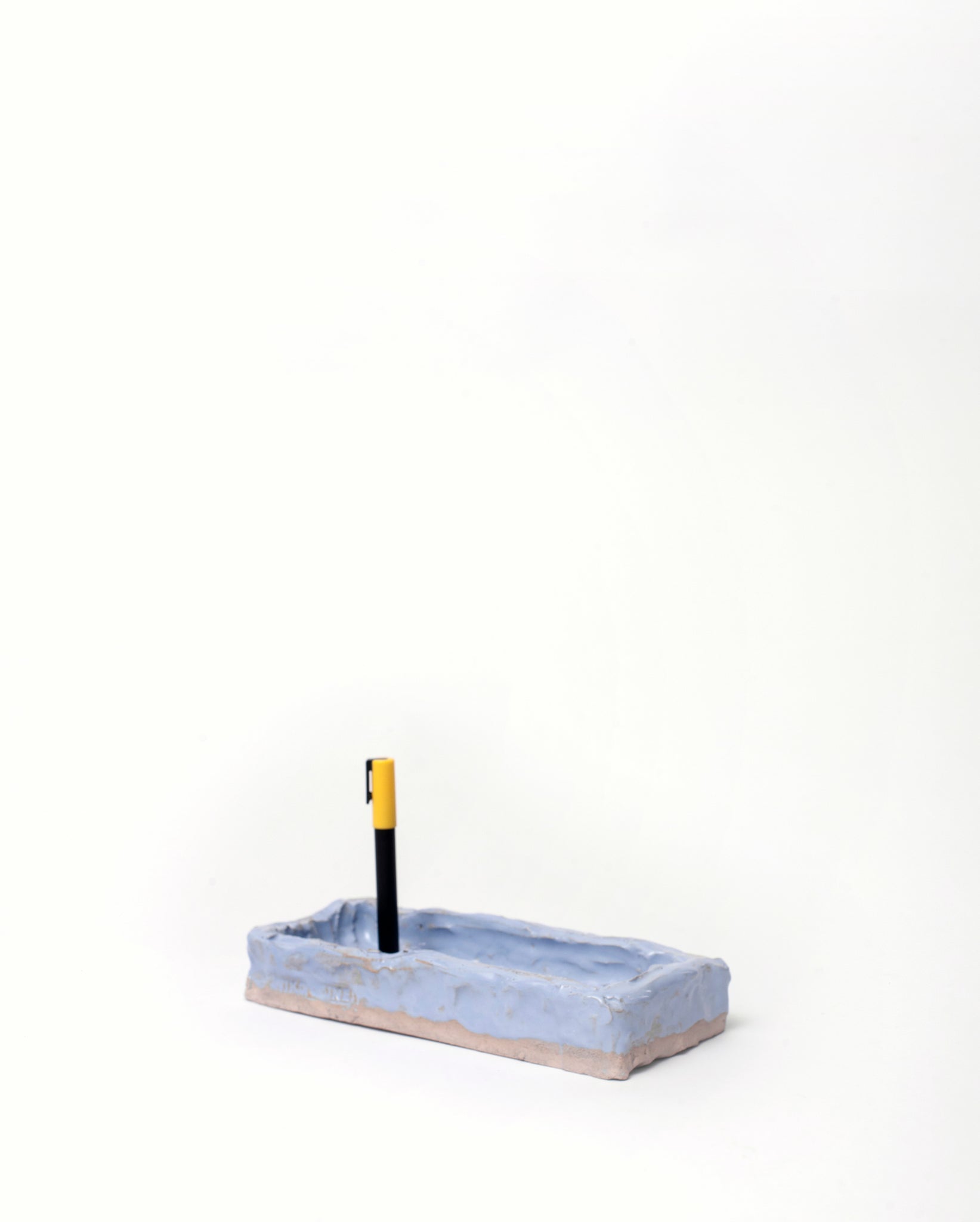 Handmade ceramic organizer object in light blue glaze with pen in one corner white background