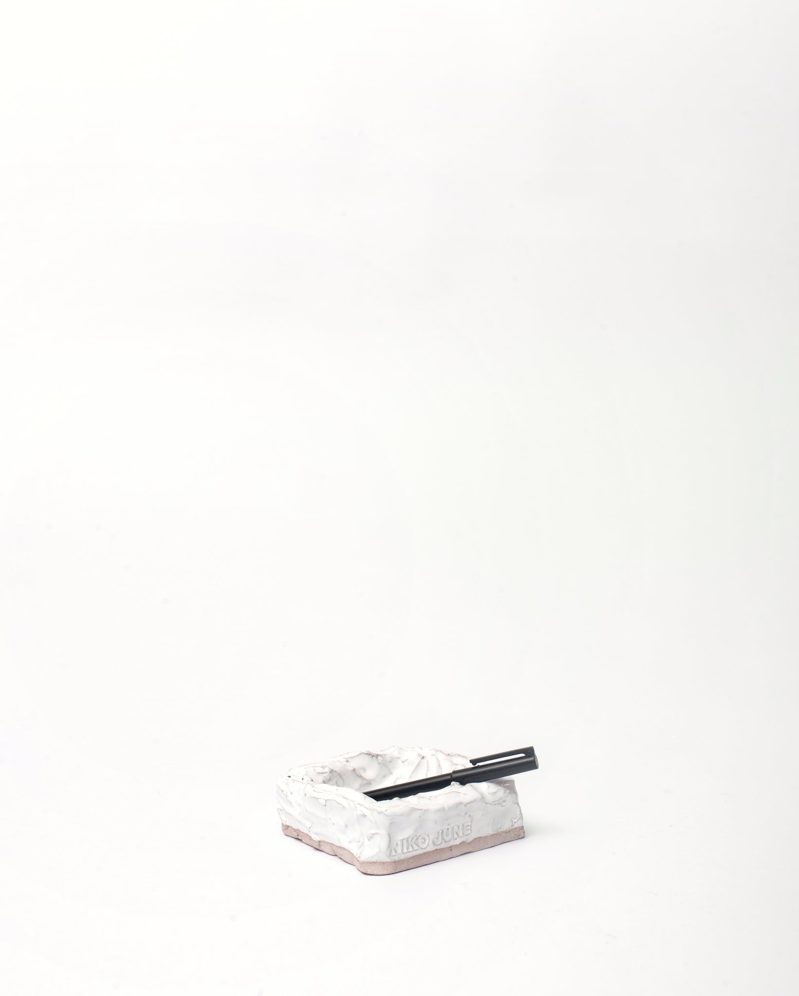 White background, Handmade jewelry ceramic organizer white in vertical inclination with black pen lying on its side