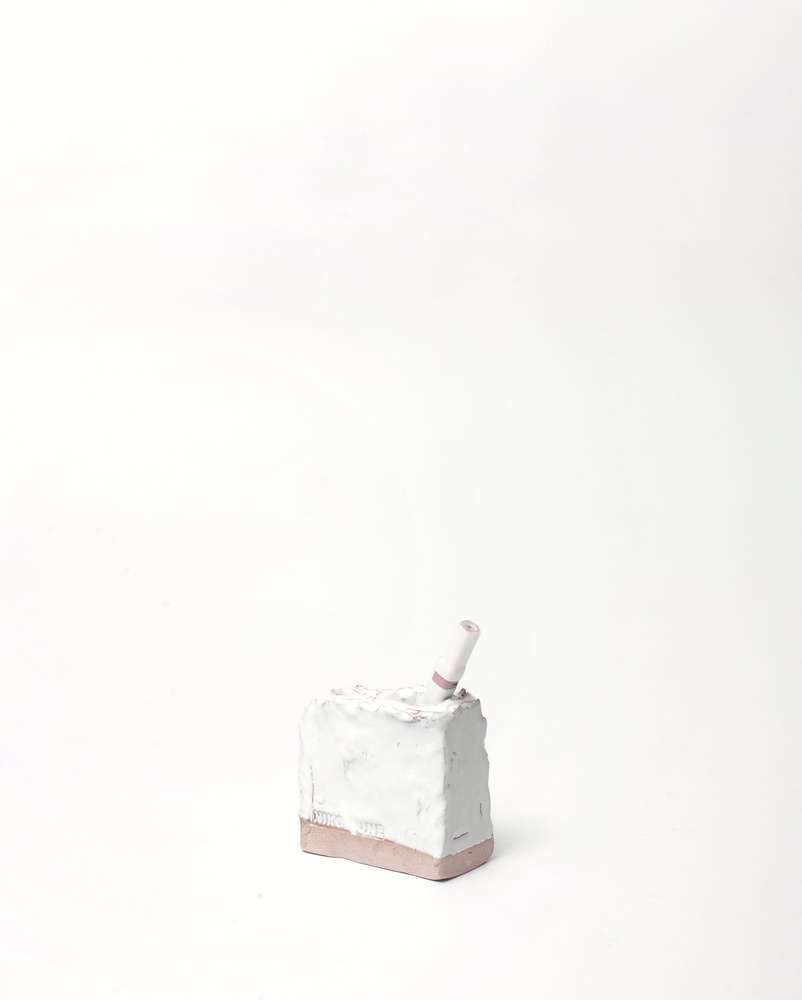 Handmade ceramic organizer object in white glaze in vertical inclination with a pen inside in white background